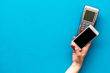 Female hand with mobile phone near POS payment terminal. Payment by mobile pay