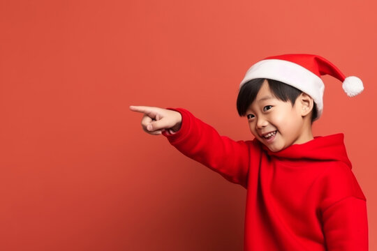 Asian kid with christmas hat pointing to blank space on red background. Generative AI