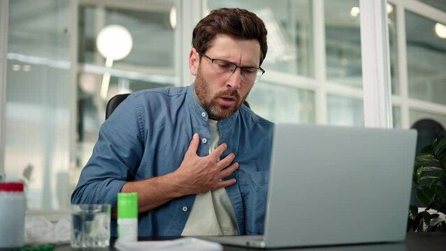 Chest pain, trouble breathing. Closeup of working bearded man in glasses, difficulty breathing or chest pain, touches his chest with hand. Heart attack, thoracic osteochondrosis, panic attack concept.