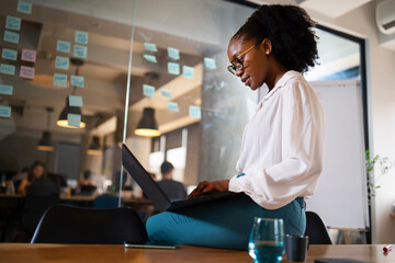Black businesswoman working on laptop. Portrait of beautiful businesswoman sitting on the desk..