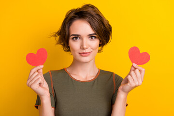 Portrait of grateful gorgeous woman with short hairdo wear khaki top hands hold two small hearts isolated on yellow color background