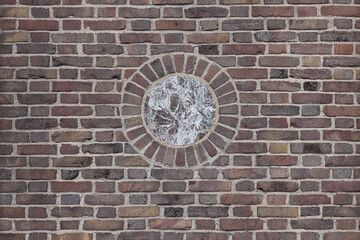 multi-colored brick wall with a brown and white marble circular medallion in the center, flemish bond bricklay pattern in earth tones, beige, brown, terra cotta, ochre, background