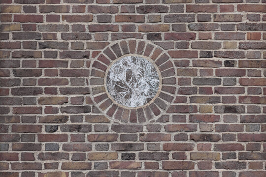 multi-colored brick wall with a brown and white marble circular medallion in the center, flemish bond bricklay pattern in earth tones, beige, brown, terra cotta, ochre, background