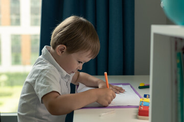 Naklejka na ściany i meble a preschooler draws at home sitting at a desk, a workplace for a child