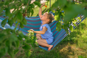 A pretty girl is sitting on a hammock in the rays of the contour light waving a carrot with a stem above her