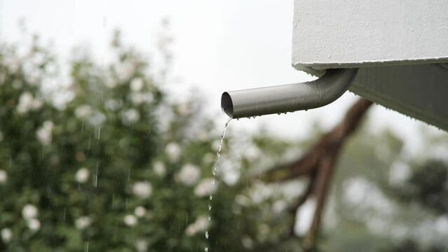 Rain water flowing from a house roof rain gutter or drain pipe. Low angle view, close up telephoto shot, selective focus, slow motion, no people