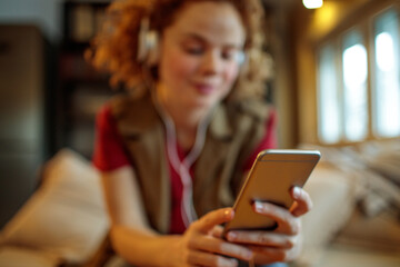 Young woman using a smart phone and listening to music on the couch in the living room
