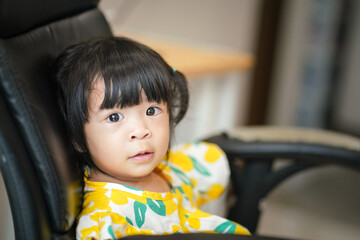 A cute caucasian baby girl with big eyes and black hair in bright yellow dress, looking to the camera. People portairt photo.