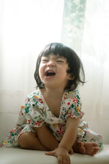 A cute caucasian baby girl with big eyes and black hair in white colorful dress, looking to the camera. People portairt photo.