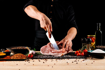 Chef cutting meat with a knife on kitchen table. Cooker is making a meal out of beef and vegetables on professional kitchen 