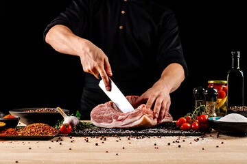 Chef cutting meat with a knife on kitchen table. Cooker is making a meal out of beef and vegetables on professional kitchen 