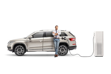 Full length portrait of a man leaning on a SUV plugged into an electric vehicle charging station