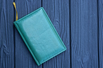 one small closed green notepad with leather cover lies on a black wooden table