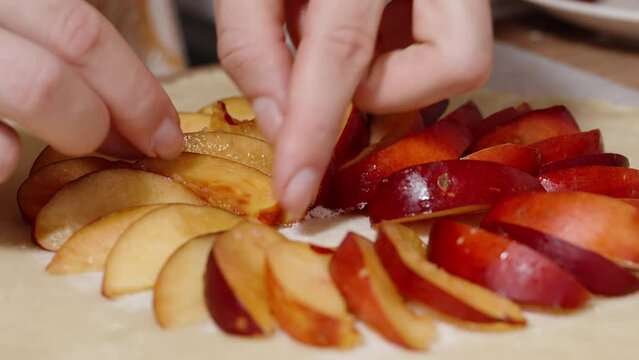 A woman is making a nectarine pie, placing slices in a circular pattern on the dough.