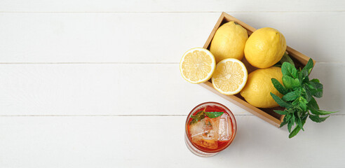 Glass of ice tea and box with lemons on white wooden background with space for text, top view
