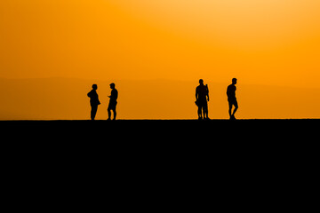 Fototapeta na wymiar Silhouette of tourists on a sea wall watching a spectacular orange sunset