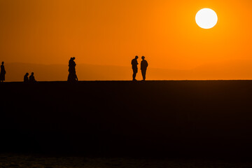 Fototapeta na wymiar Silhouette of tourists watching the sun set behind a distant mountain in summer