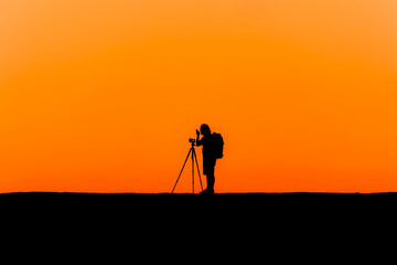 Silhouette of a lone photographer with tripod taking an image during a beautiful orange sunset