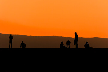 Fototapeta premium Silhouette of tourists on a sea wall watching a spectacular orange sunset