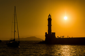 Silhouette of a lighthouse and small yacht during a beautiful golden sunset on a Greek island in summer