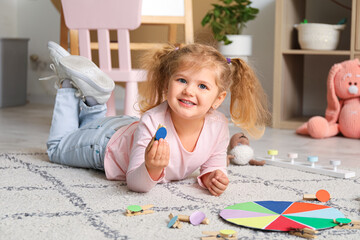 Cute little girl playing matching game with clothespins on floor at home