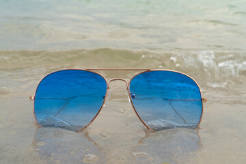 Blue sunglasses lie in the sand on the beach near the sea. Summer vacation, travel and tourism concept