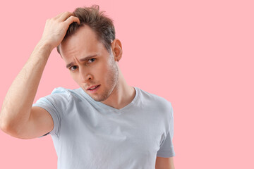 Upset young man with hair loss problem on pink background