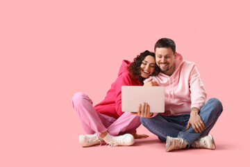 Young couple using laptop on pink background