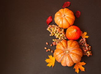 Border made of pumpkins, autumn leaves and grapes on dark background.