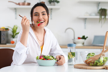 Young woman eating vegetable salad in kitchen