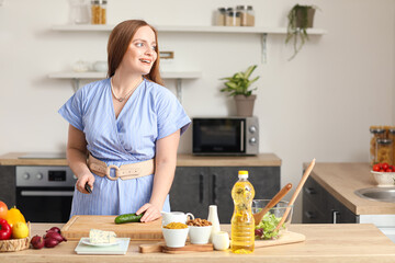 Young woman cutting cucumber for salad in kitchen