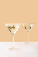 Glasses of martini with olives on beige background