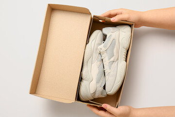 Female hands holding cardboard box with stylish shoes on beige background