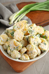 Bowl of tasty Potato Salad with greens on grey background