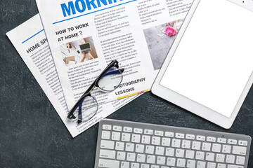 Obraz premium Tablet computer with newspapers, eyeglasses and keyboard on dark background
