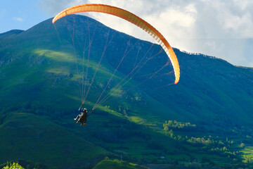 Paragliding team flying over the green mountain slope at summertime evening backlit by sun. Paraglider fly over mountains on sunny summer day in France