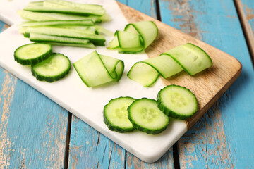 Board with fresh cut cucumber on blue wooden background, closeup