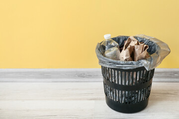 Plastic trash bin with different garbage near yellow wall