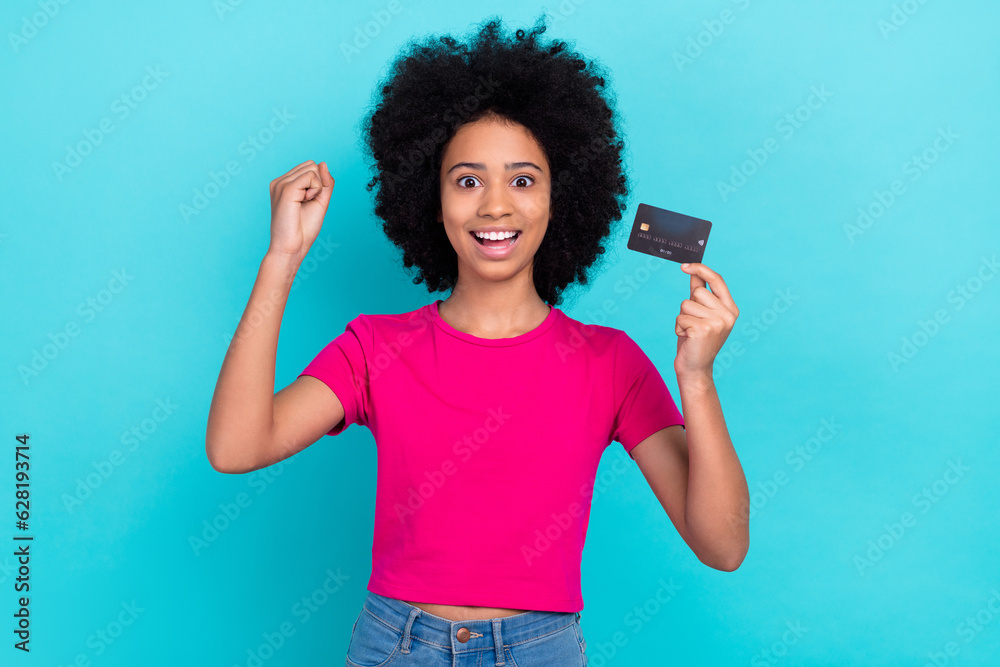 Sticker Photo of charming overjoyed girl with afro chevelure wear pink t-shirt hold credit card go shopping isolated on blue color background