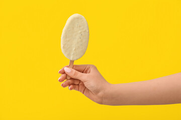 Fototapeta na wymiar Woman holding delicious chocolate covered ice cream on stick against yellow background