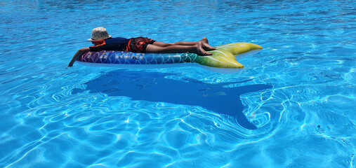 
The child floats on an inflatable mattress in the pool. Summer vacation for a family with children in the water park. A boy floats on an inflatable mattress in a clean swimming pool in a hotel.
