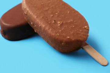 Delicious chocolate covered ice cream on stick against blue background, closeup