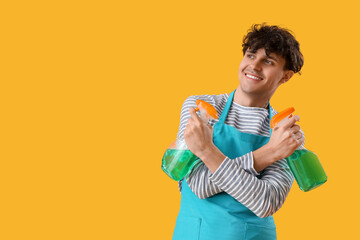 Young man with spray bottles of detergent on yellow background