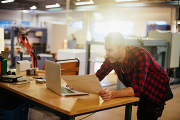 Young man using a laptop while working in a printing press office