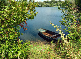 Altes, verlassenes, rostiges Ruderboot am Ufer von einem idyllischen kleinen See im Sommer.