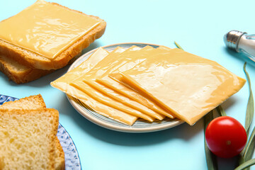 Plates of tasty processed cheese with bread and vegetables on blue background