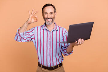 Photo of cheerful pensioner man arm hold netbook fingers demonstrate okey symbol feedback isolated on beige color background