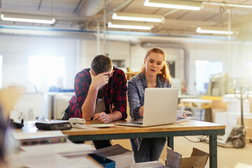 Young man and young woman using a laptop while working in a printing press office