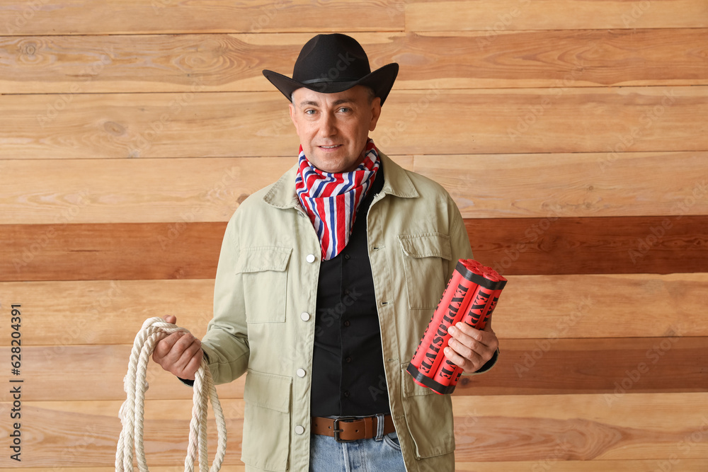 Poster Mature cowboy with lasso and explosive on wooden background