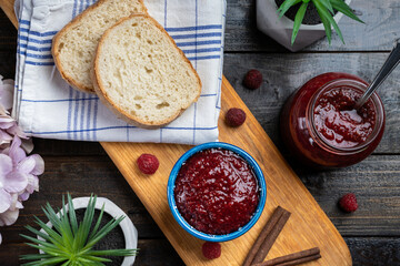 Fresh homemade raspberry jam in a bowl served on a wooden platter with bread